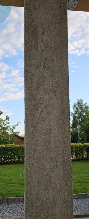 Betongpelare med obrutet ytterskikt, tagen utomhus mot en bakgrund av grönska och blå himmel.