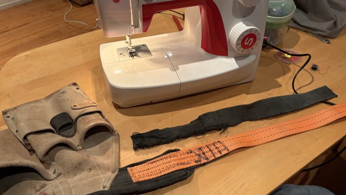 Symaskin på bord med ett slitet snickarbälte och ett nytt spännband på väg att sys fast som midjerem.