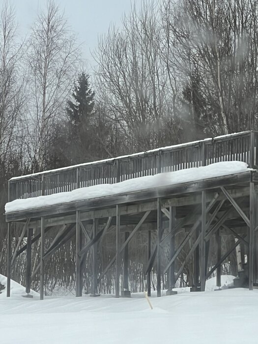 Altan av trä, täckt med snö, med stödben i vintermiljö.