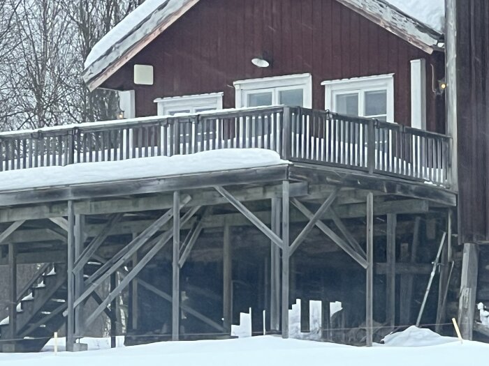 Altan till rött hus i vinter, byggd på höga stolpar med snö på räckena, ser instabil ut enligt diskussionsinlägget.