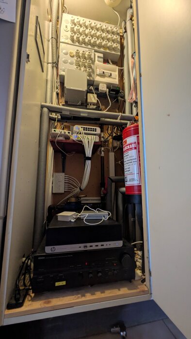 Skåp med förstärkare, dator, nätverksutrustning och brandsläckare; visar hur utrymmet organiserats för att optimera ventilation.