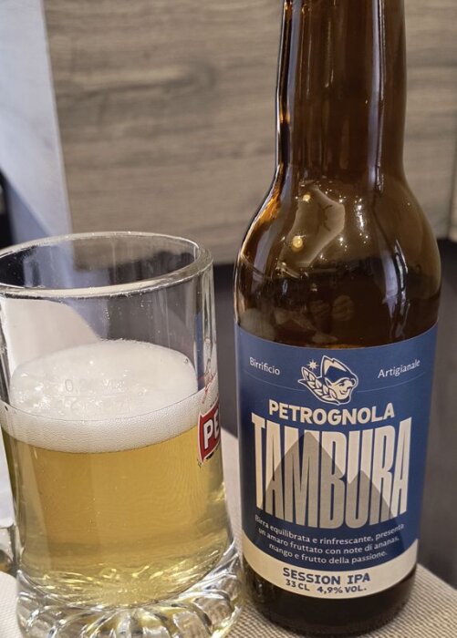 Flaska av Petrognoła Tamura Session IPA bredvid ett ölglas med skummande öl.