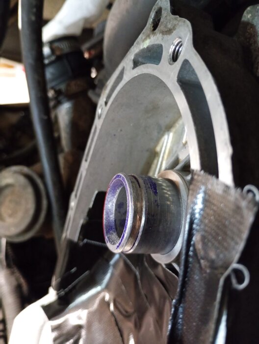 Närbild på en bilmotor med ett monterat lager och distansring på en axel, omgivet av metall och ledningar i ett trångt utrymme.