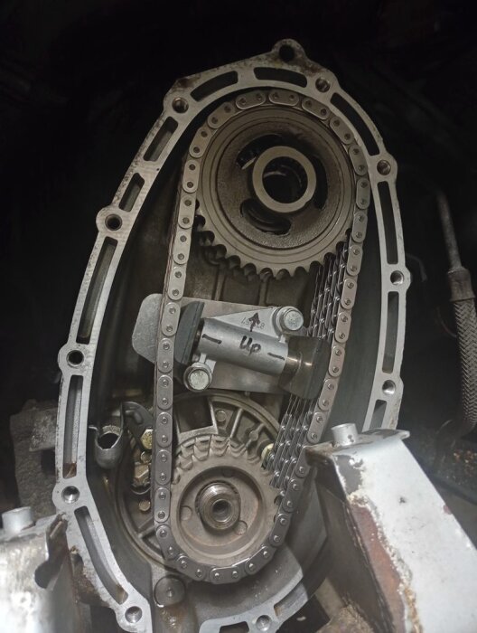 Växelkåpa på ett bilens motor där nya kedjor och en spännare har installerats, med synliga kugghjul och distansringar.