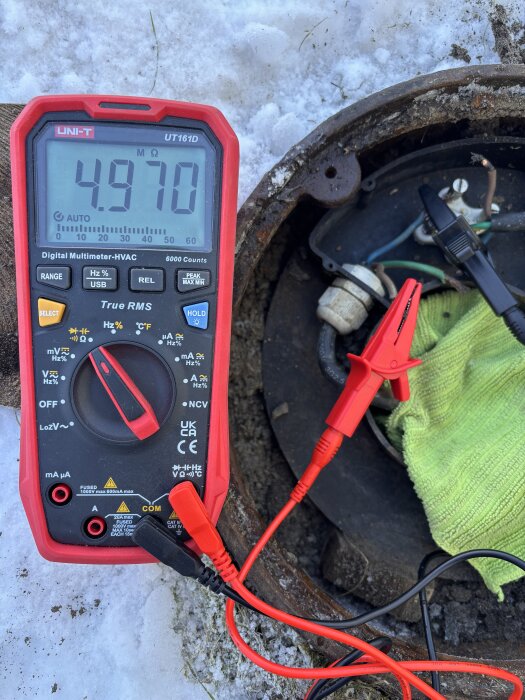 Multimeter visar 4970 ohm vid mätningar nära pumphålet, omgiven av snö och kablar.