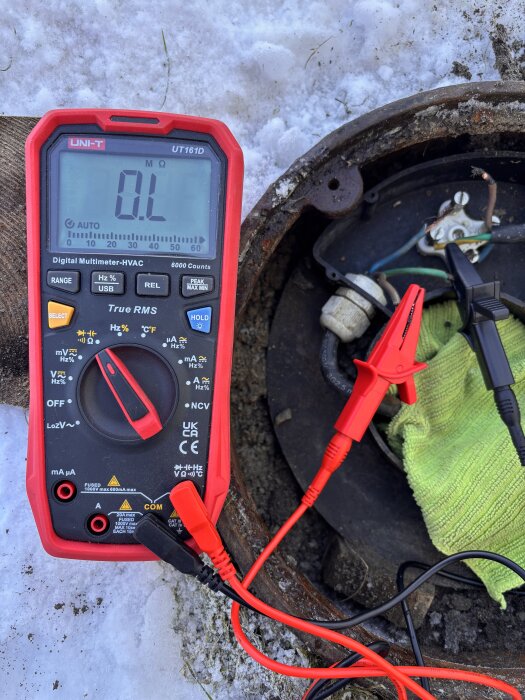 Multimeter visar 0L vid pumphål, omgiven av snö och anslutna kablar.