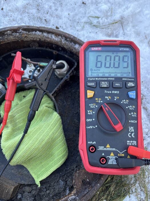 Digital multimeter visar 60 MΩ med ledningar anslutna vid en kopplingsdosa nära snö.