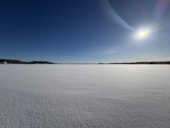 Solig vy över Trälhavet på en snötäckt dag med klar blå himmel och skog i fjärran.