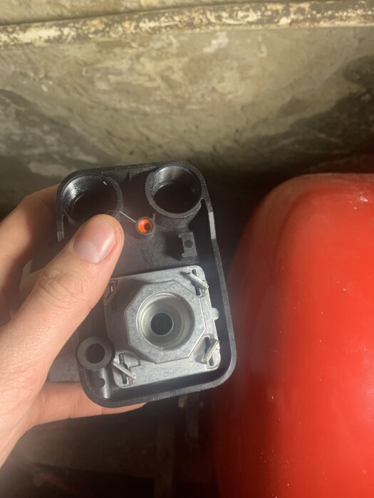 Tryckströmbrytare med synlig adapter och mutter, hålls i en hand mot en betongvägg.