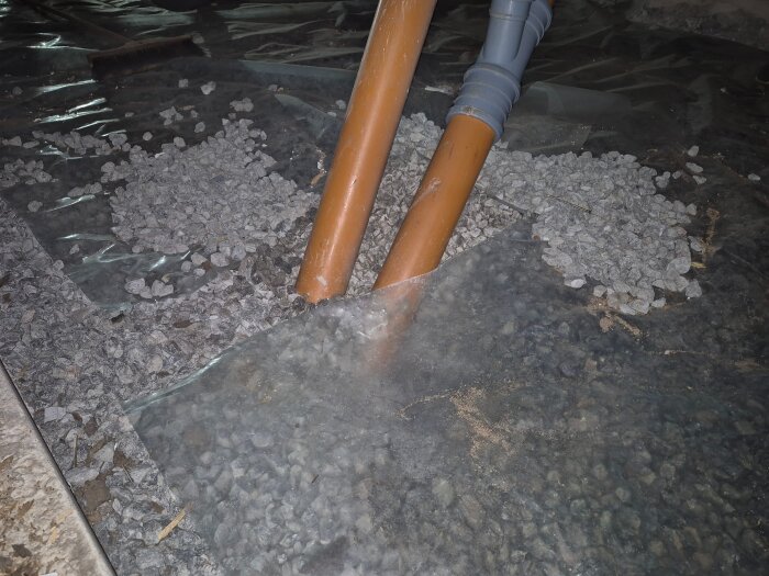 Plastfolie i krypgrund med orange avloppsrör och synligt makadam, delvis täckt av plasten.