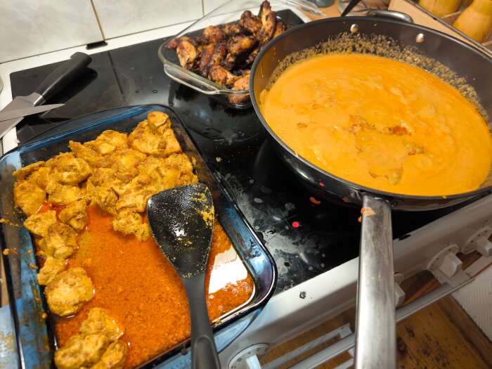 Matlagningsscen med kyckling Tikka Masala och honungsvingar på en spis, med en gryta fylld med sås och en form med kyckling.
