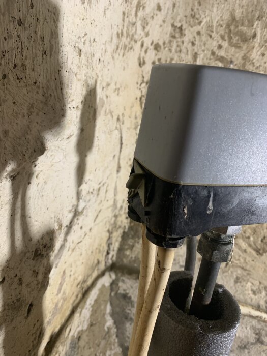Anslutning av rör och kablar vid en vägg, med fokus på en monterad enhet utan muttrar, i en bygg- eller renoveringssituation.
