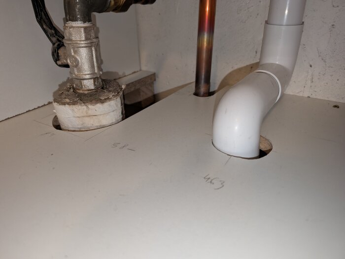 VVS-installation med rörgenomföring i en köksbänk, visar koppar- och plastledningar genom hål markerade med mått.