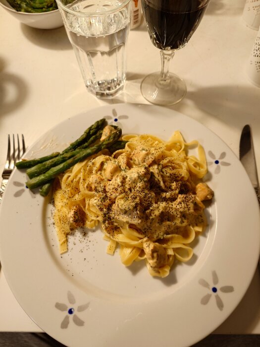 Tallrik med lax, pasta och sparris, serverad med glas rött vin och vatten.