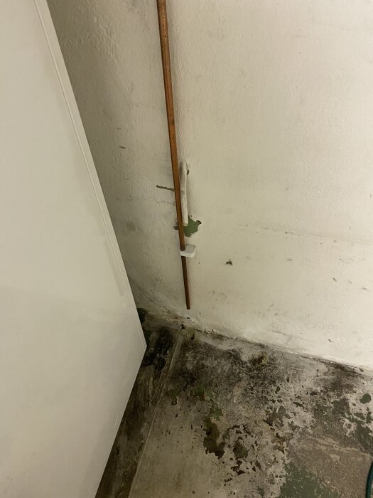 En kopparrör mot en vägg med fuktmärken på golvet.