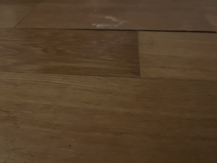 Skadat parkettgolv med synliga springor och ojämn yta, potentiell fuktskada och behov av reparation eller byte av träbitar.