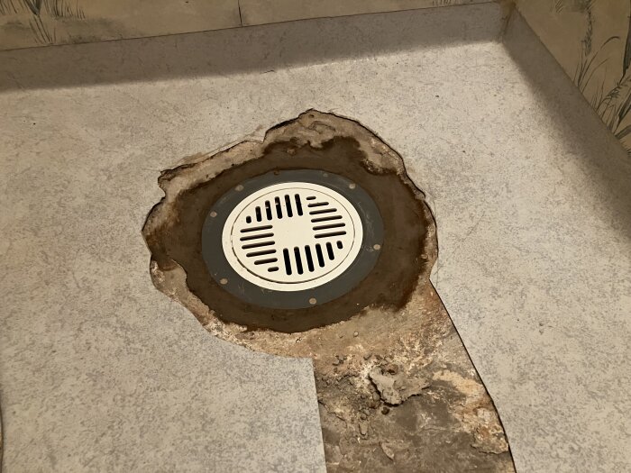 Nyinstallerad golvbrunn i ett duschrum, omgiven av uppskuren våtrumsmatta med exponerad betong.
