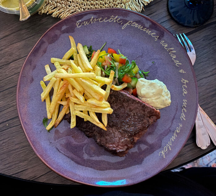 Entrecôte med pommes frites, sallad och bearnaisesås på en tallrik med inskription, serverad på ett mörkt träbord.