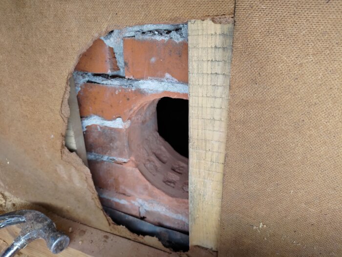Hål i vägg med tegel och trä synliga, förberett för installation av spirorör i renoveringsprojekt av köksventilation.