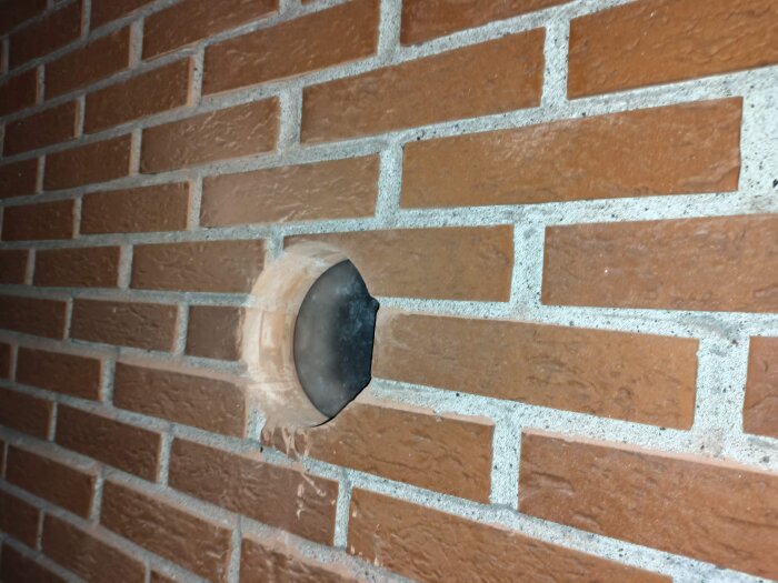 Hål i tegelvägg med nyligen installerat 160mm spirorör för köksventilation, omgärdat av borrdamm och vinkeljärnsförstärkning.