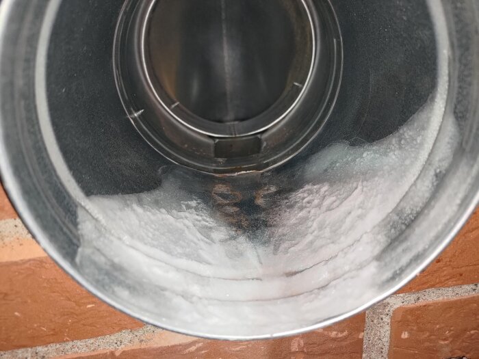 Närbild av en insida av ett 160 mm spirorör för ventilation, med synliga kondensdroppar på rörväggen, monterad genom en tegelvägg.