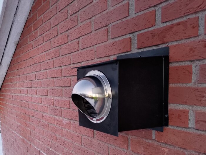 Ventilationshuv i rostfritt stål monterad på en röd tegelvägg.