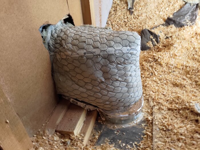 Isoleringsmaterial täckt med nät och märkt "Paroc" installerat i en väggyta med träspån på golvet.