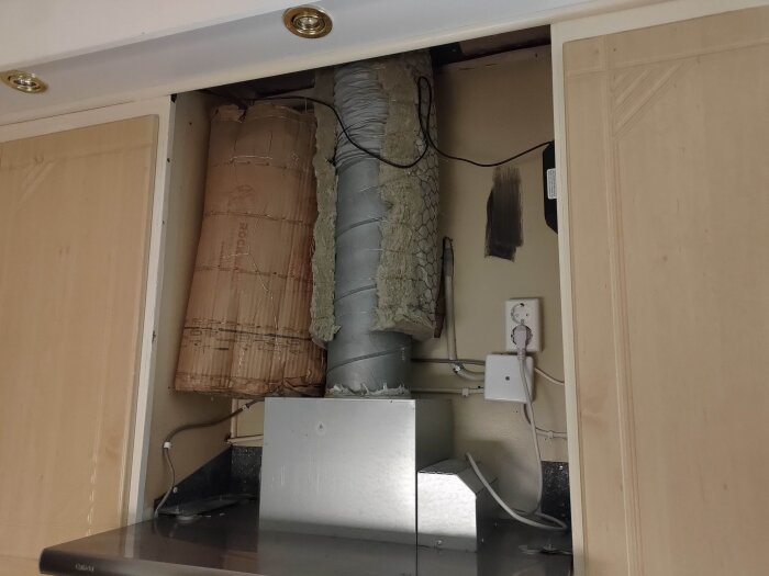 Öppen köksskåpsinstallation med fläktkåpa, isolerad ventilationskanal och eluttag.