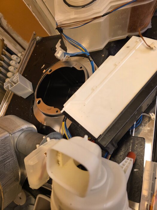 Delar från en isärplockad diskmaskin, inklusive ledningar och plastkomponenter, ligger utspridda inuti maskinen.