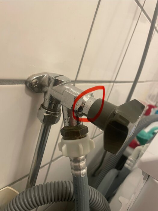 Vattenrörsanslutning med svart vred, markerat med röd cirkel, visar område där det droppar vatten mellan vredet och muttern.