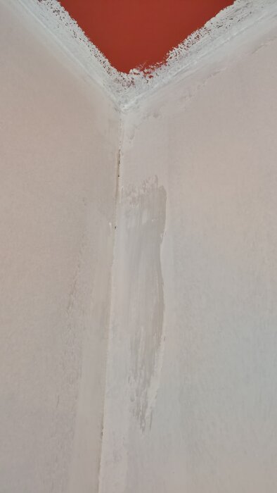 Hörn av ett rum med ojämnt applicerad spärrfärg och bristande målning i hörnen. Tydliga tecken på rinnande färg från taket.