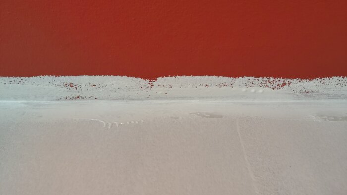 Detaljbild av en vägg som nyligen har spärrmålats, med ojämt tjocka lager och färgstänk på den röda väggen ovanför.