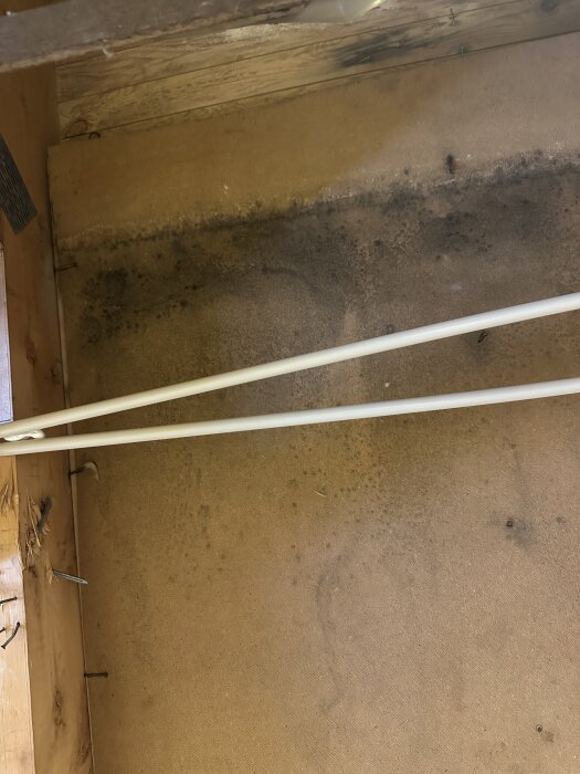 Masonitskiva med mörka fläckar, potentiellt mögel, i ett rum under renovering, med två vita rör i förgrunden.