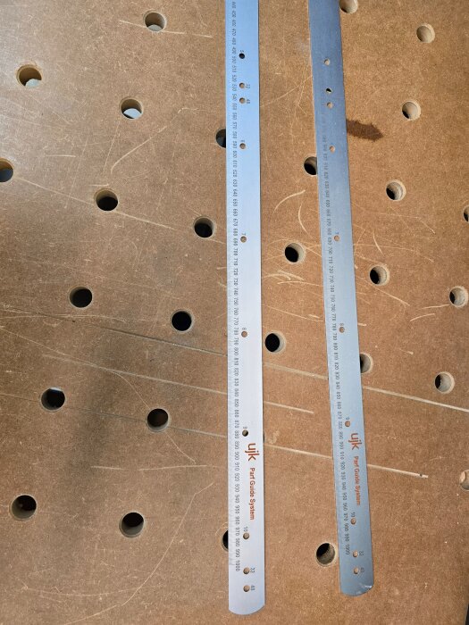 Två metallinjal för UJK Parf Guide System på en träskiva med hål, används för att tillverka exakta 20 mm hålskivor.