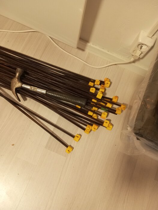 Gulmarkerade märkpinnar och en hammare ligger på ett ljust trägolv nära ett eluttag.