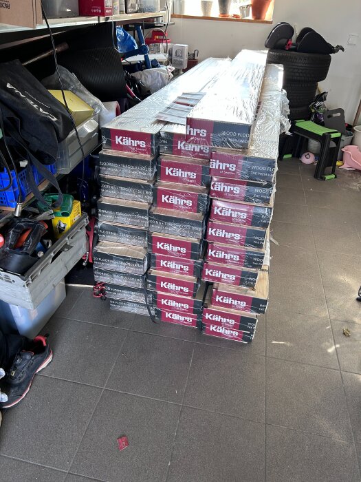 Staplar med Kährs Verona tvåstavig parkett inslagna i plast, lagrade i ett garage tillsammans med verktyg och andra föremål.