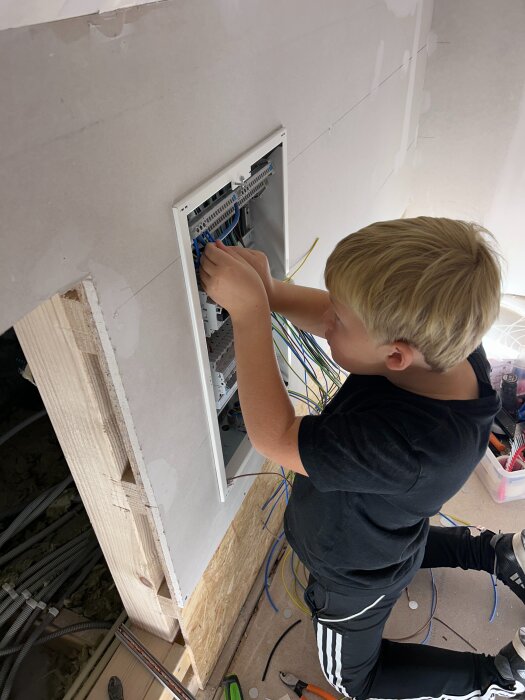 Barn hjälper till med elinstallation genom att koppla kablar i en elcentral på en byggarbetsplats.