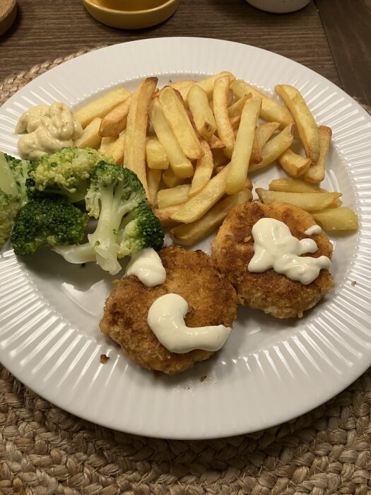 Tallrik med laxbiffar toppade med sås, pommes frites och broccoli. En klick remouladsås vid sidan om.
