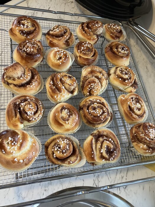 Kanelbullar som nyss gräddats, placerade på ett galler med pärlsocker på toppen, på ett marmorbord.