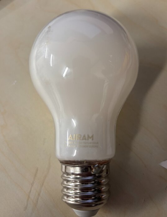 E27 dimbar glödlampa med märket "Airam" syns på ett bord, med text och symbols på ytan.