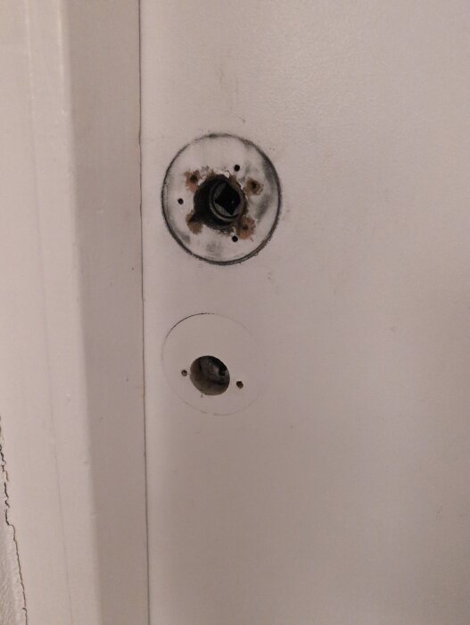 Närbild på en innerdörr med borttagen dörrhandtagsskylt, exponerade skruvhål och gångjärn synliga på innersidan.