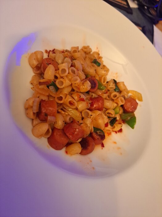 Pasta med korvbitar, lök, vitlök, salladslök och paprika på en tallrik.
