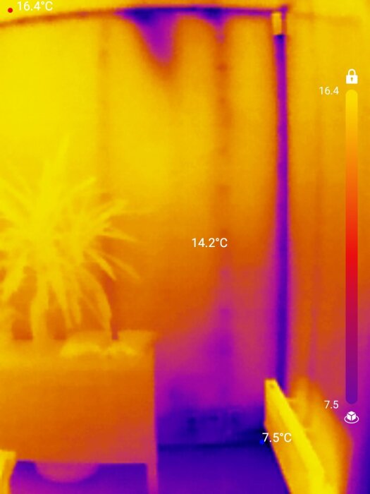 Termisk bild av en yttervägg med temperaturvariationer, visar värmeläckage och kalla områden runt en dörr och växt, taget med en Topdon tc001 kamera.