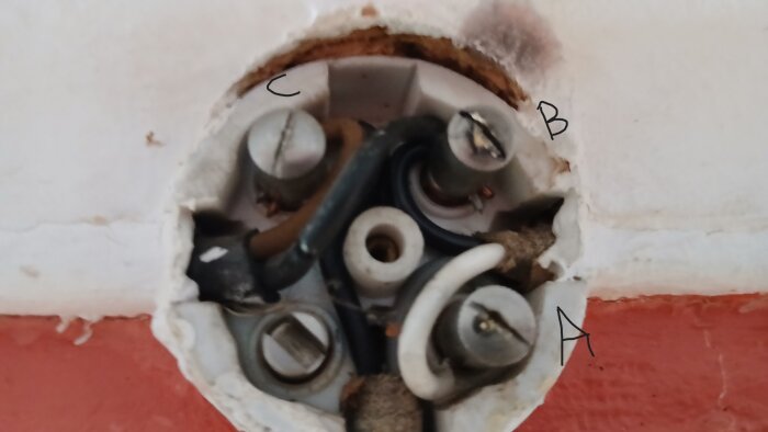 Kopplingsdosa i vägg med tre märkta anslutningspunkter (A, B, C) och flera elektriska kablar anslutna.