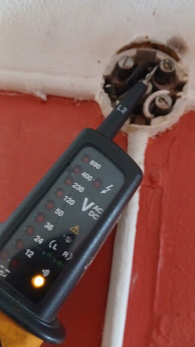 Spänningsmätare visar 230V på kopplingspunkt; kablar och vägg synliga i bilden.