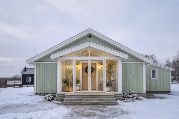 Grönt hus med glasad entré på kortsidan, dekorerad med växter och ljus under vintern.