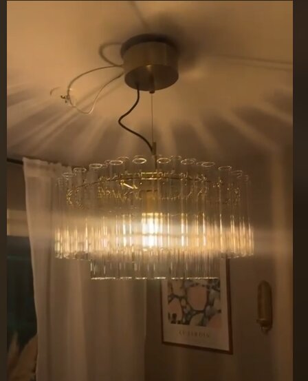 Modern takkrona med glasdetaljer installerad i taket med sladdar synliga, omgiven av inredning och belysning som sprider sig på taket.