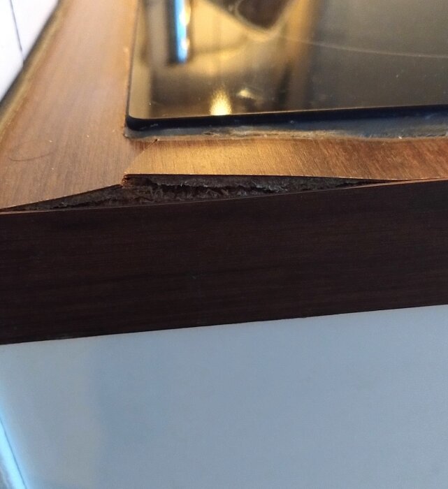 Skadad kant på en brun köksbänk bredvid en inbyggd spishäll.