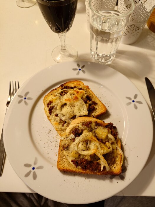 Varma mackor med köttfärs, ananas, lök och ost på en tallrik, serverade med glas vatten och dryck.