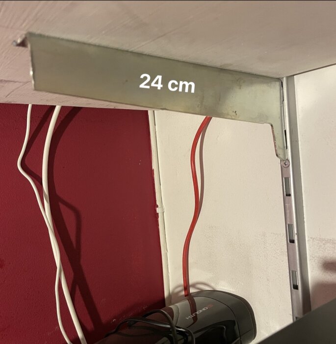 Metallkonsol 24 cm monterad på väggskena mot röd och vit vägg, med röd och vit kabel intill.